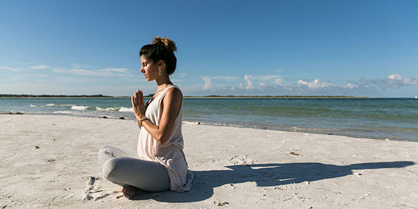 A young woman meditates to improve her wellness on a pristine sandy beach